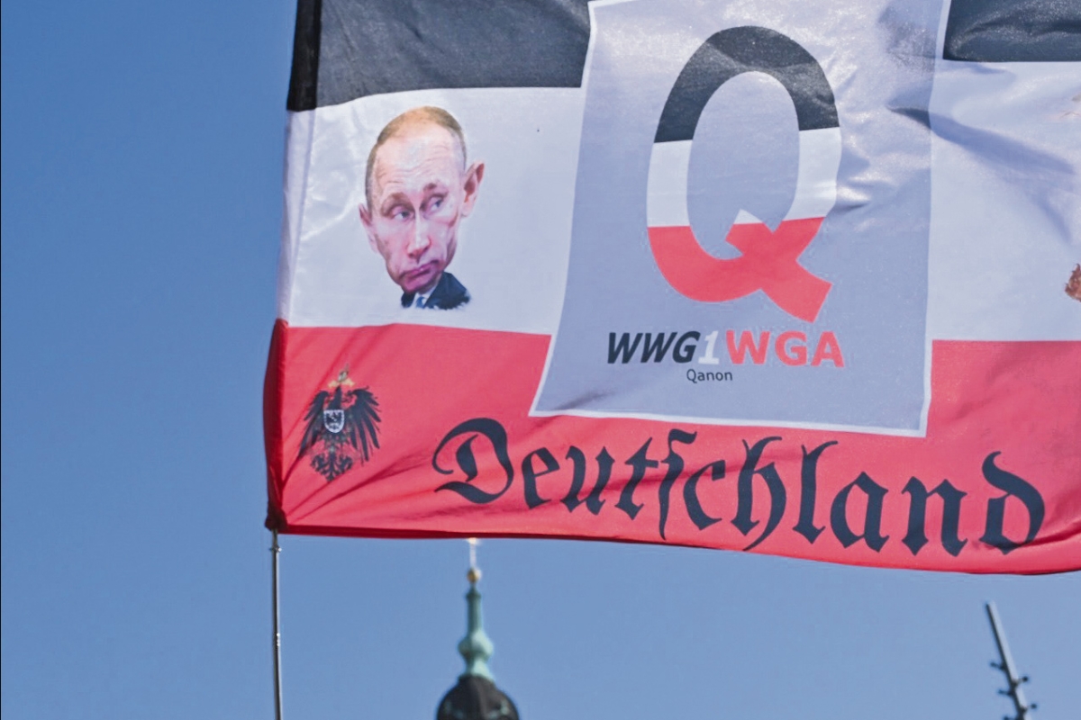 Fahne in schwarz weiß rot mit Deutschland in Frakturschrift, einem großen Q in der Mitte und einer Zeichnung von Putin auf der linken Seite