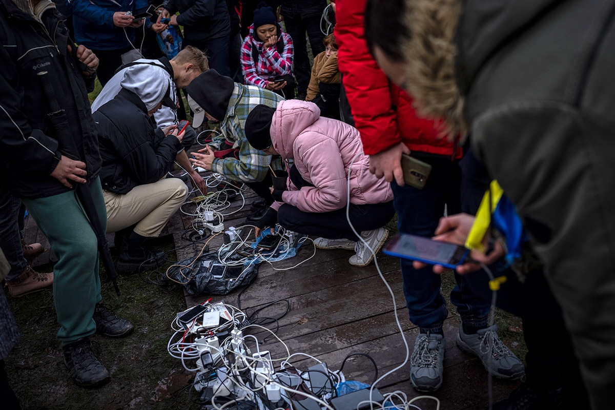 An Kabelknäueln und Mehrfachsteckern auf dem Boden laden Menschen ihre Telefone