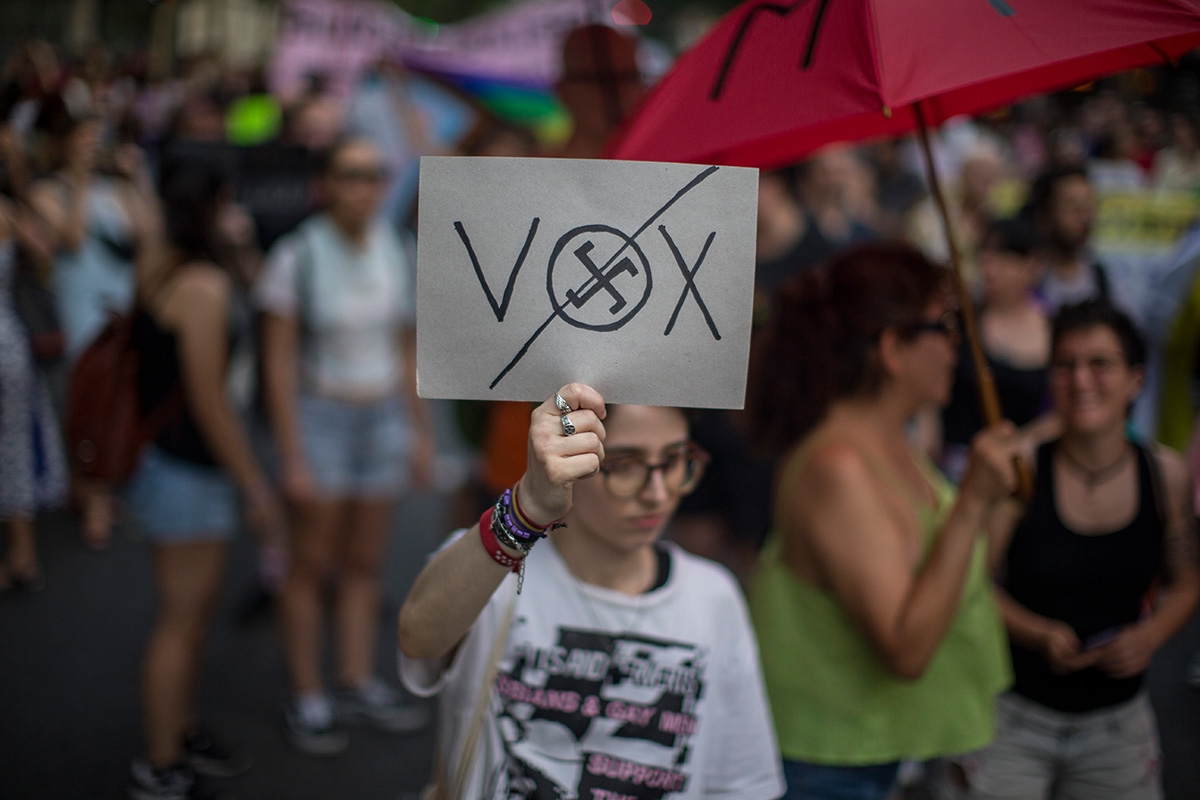 Demonstrantin mit Schild, auf dem"Vox" durchgestrichen und im O von Vox ein Hakenkreuz zu sehen ist