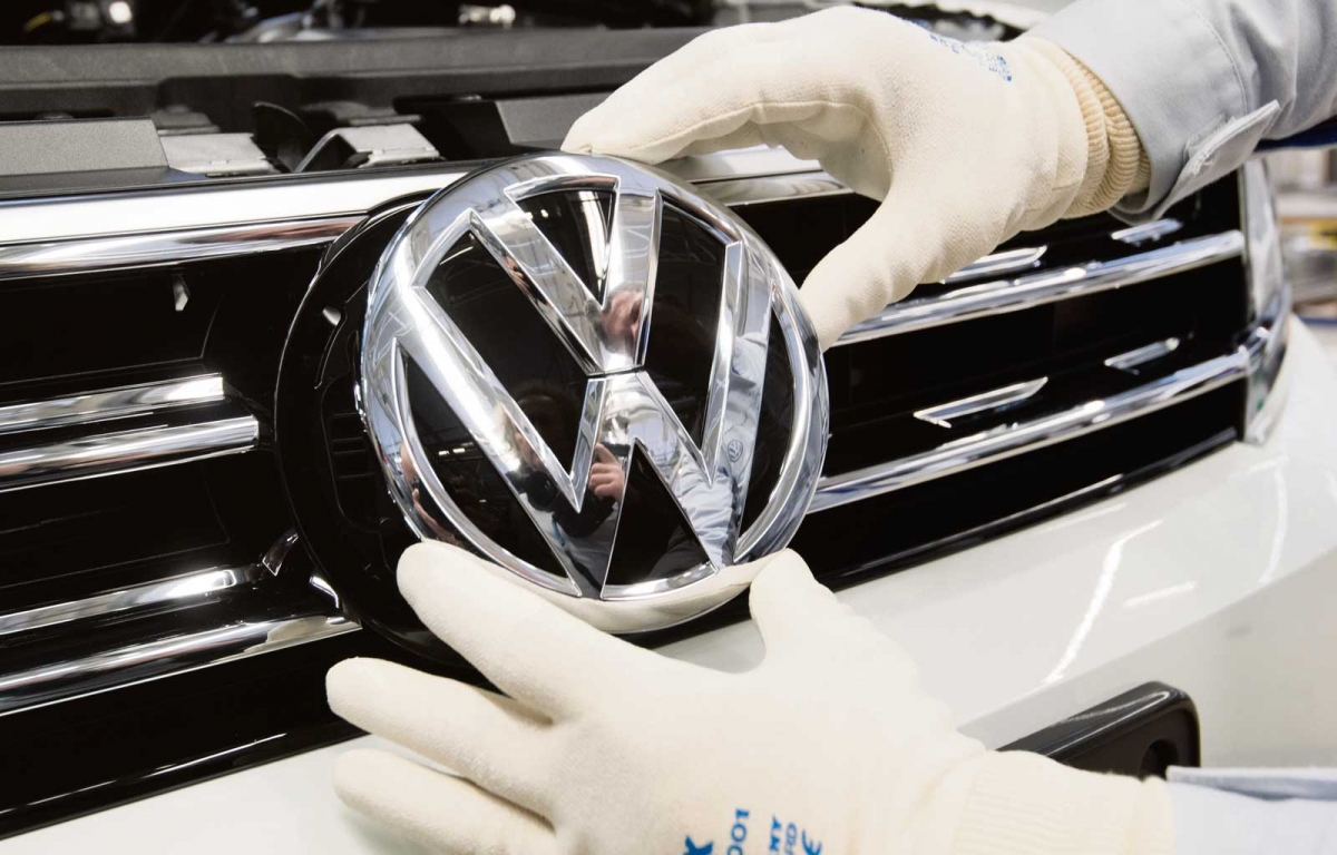 Ein Mitarbeiter montiert das VW-Logo an einen Neuwagen, Wolfsburg, 1. März