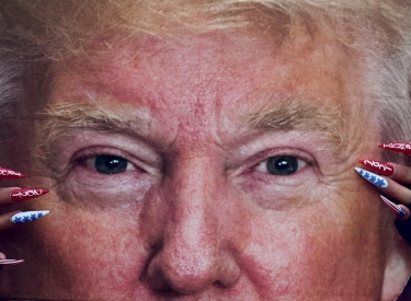 Person mit langen Fingernägeln hält ein Plakat von Trumps Kopf