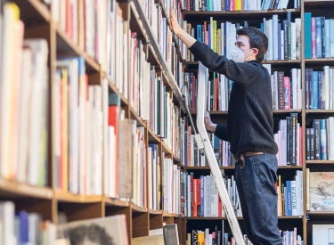 Mitarbeiter einer Buchhandlung der Walther-König-Kette steht auf einer Leiter vor einem großen Bücherregal