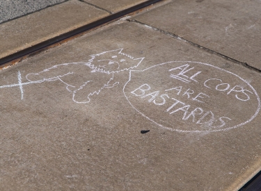 Kreidezeichnung auf Straße zeigt einen Hund mit Sprechblase: All Cops Are Bastards